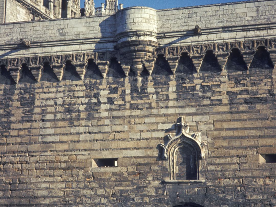 The curtain wall of the Château des ducs de Bretagne at Nantes, machicolations along the parapet and a barred window low in the stone.