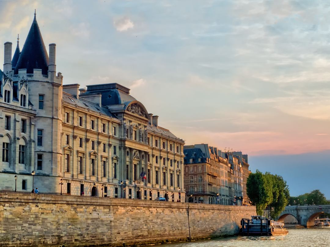 The Seine at dusk in Paris, the arches of the Pont Neuf and the long stone frontage of the Île de la Cité under a pink sky.